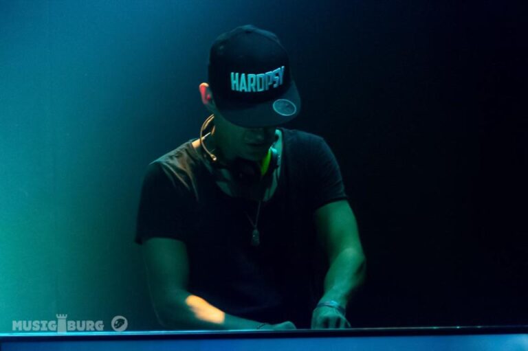 Ein DJ mit Kappe, der an einem Mischpult in einem dunklen Club mit gedämpfter Beleuchtung Musik mixt.